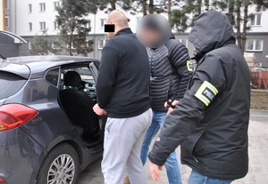 Nieumundurowani policjanci prowadzą do samochodu zatrzymanego sprawcę rozboju.