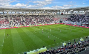 Stadion przy aleii Uni Lubelskiej, podczas meczu piłkarskiego. Na murawie piłkarze obu drużyn, na trybunach kibice.