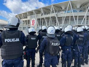 Policjanci w kaskach i kamizelkach odpornych na uderzenia stoją przed stadionem.