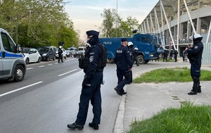 Policjanci i radiowozy oznakowane stoją wokół stadionu.