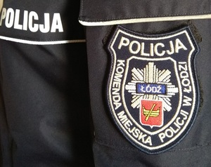 Mundur policyjny, na rękawie naszywka z napisem Komenda miejska Policji w Łodzi, policja oraz herbem Łodzi i odznką policyjną.