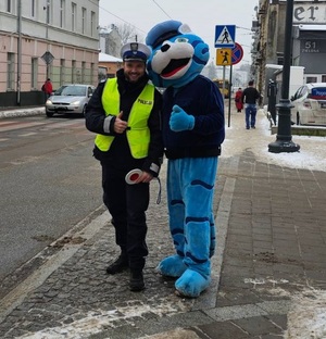 Policjant ruchu drogowego z maskotką łódzkiej Policji Kotem Prewencjuszem, stoją na chodniku.