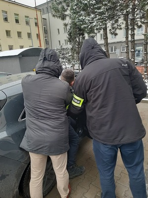Policjanci pomagają wsiąść zatrzymanemu do radiowozu.