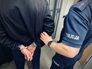 Policjant trzymający zatrzymanego, który ma założone kajdanki na ręce.