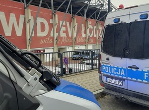Oznakowane radiowozy policyjne, w tle stadion Widzewa Łódź.