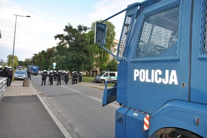 Policyjna armatka wodna, w tle policjanci czekający na przyjazd pociągu specjalnego z kibicami.