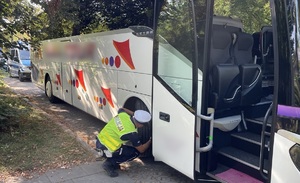 Policjant z drogówki kontroluje stan techniczny autobusu.