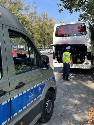 Policjant z drogówki kontroluje stan techniczny autobusu.