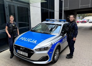 Umundurowane policjantki stoją koło oznakowanego radiowozu.