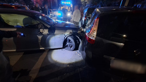 Auta uszkodzone podczas kolizji, w tle radiowóz policyjny na sygnałach uprzywilejowania.