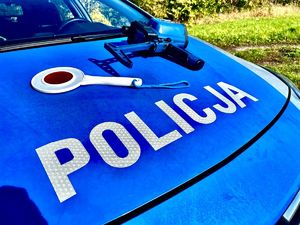 Na masce oznakowanego radiowozu policyjnego leży ręczny laserowy miernik prędkości oraz tarcza do zatrzymywania pojazdów.
