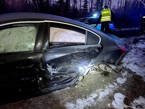 Uszkodzony pojazd, w tle radiowóz policyjny i policjant z Wydziału Ruchu Drogowego.