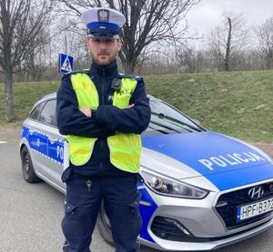 Policjant Wydziału Ruchu Drogowego Komendy Miejskie Policji w Łodzi stoi przed radiowozem.