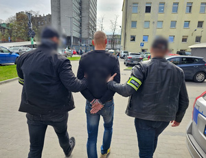 Policjanci prowadzą zatrzymanego mężczyznę.