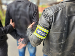 Policjanci trzymają mężczyznę, który ma kajdanki założone na ręce trzymane z tyłu.