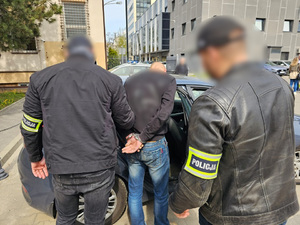 Policjanci pomagają zatrzymanemu mężczyźnie wsiąść do radiowozu.