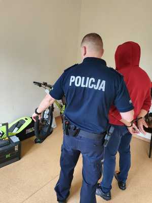 Policjant z zatrzymanym, w tle zabezpieczone przedmioty.