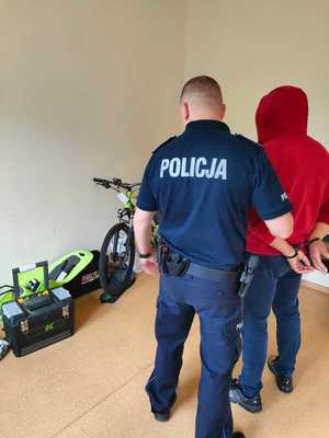 Policjant z zatrzymanym, w tle zabezpieczone przedmioty.