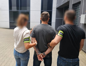 Policjantka i policjant trzymają mężczyznę, który ma kajdanki założone na ręce z tyłu.
