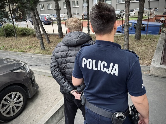 Policjant prowadzi zatrzymanego mężczyznę.