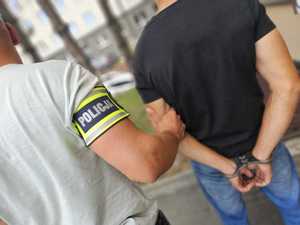 Policjant trzyma mężczyznę, który ma założone kajdanki na ręce z tyłu.