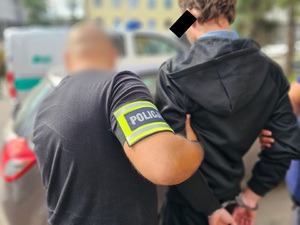 Policjanci pomagają zatrzymanemu mężczyźnie wsiąść do radiowozu.