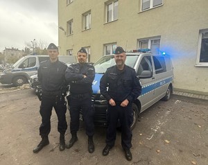 Umundurowani policjanci stoją przed radiowozem.