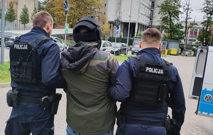 Umundurowani policjanci prowadzą zatrzymanego mężczyznę.