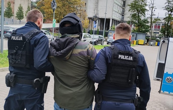 Umundurowani policjanci prowadzą zatrzymanego mężczyznę.
