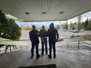 Policjanci trzymają mężczyznę, który ma założone kajdanki na ręce z tyłu.