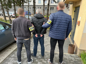 Policjanci trzymają mężczyznę, który ma kajdanki założone na ręce z tyłu.