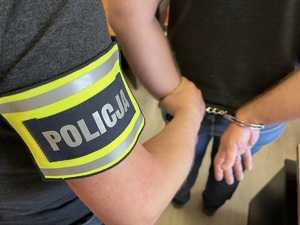 Zdjęcie poglądowe: policjant trzyma mężczyznę, który ma kajdanki założone na ręce z tyłu.