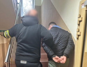 Policjant wprowadza zatrzymanego na schody.