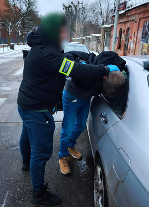 Policjant stoi z zatrzymanym mężczyzną przy samochodzie.