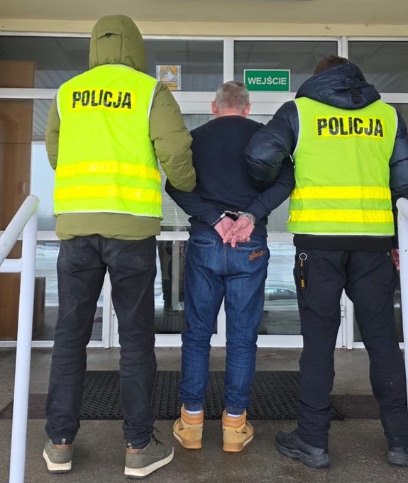 Policjanci trzymają mężczyznę, który ma założone kajdanki na ręce z tyłu.