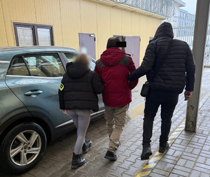 Policjanci prowadzą mężczyznę, który ma założone kajdanki zespolone.