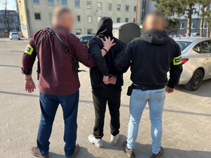 Policjanci prowadzą mężczyznę, który ma założone kajdanki na ręce z tyłu .