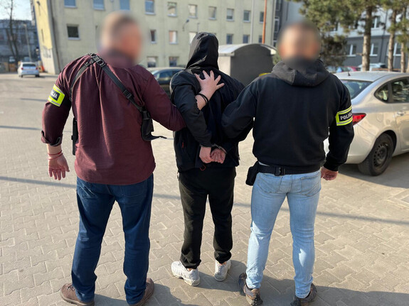 Policjanci prowadzą mężczyznę, który ma założone kajdanki na ręce z tyłu .