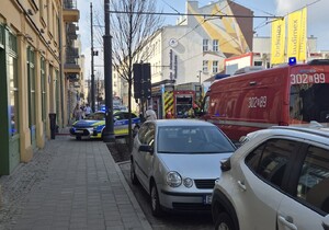 Wozy straży pożarnej i radiowóz policyjny przed kamienicą.