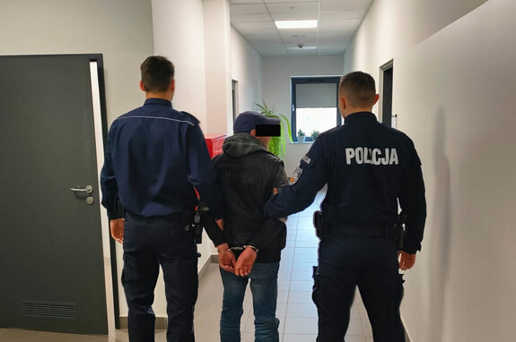 Policjanci trzymają mężczyznę, który ma założone kajdanki na ręce z tyłu.