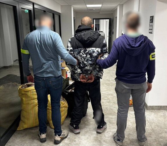 Policjanci trzymają mężczyznę, który ma założone kajdanki na ręce z tyłu.