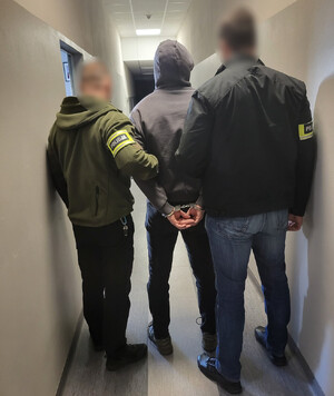 Policjanci trzymają mężczyznę, który ma założone kajdanki na ręce z tyłu.