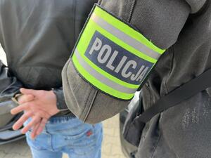 Policjant trzyma mężczyznę, który ma założone kajdanki na ręce z tyłu.