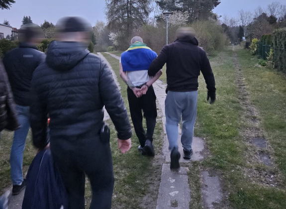 Policjanci prowadzą zatrzymanego mężczyznę.