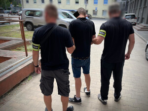 Policjanci trzymają mężczyznę, który ma założone kajdanki zespolone.