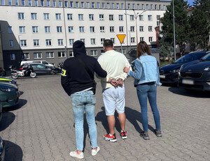Policjanci trzymają mężczyznę, który ma założone kajdanki na ręce z tyłu.