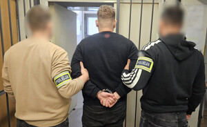 Policjanci trzymają mężczyznę, który ma założone kajdanki na ręce z tyłu.