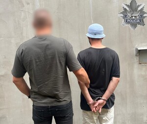 Policjant trzyma mężczyznę, który ma założone kajdanki na ręce z tyłu.