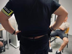 Policjant stojący przed siedzącym na krześle mężczyźnie.