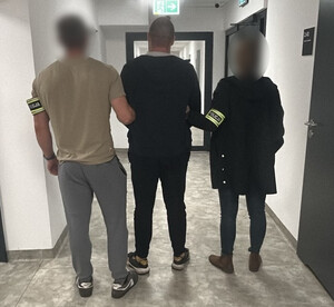 Policjanci prowadzą zatrzymanego mężczyznę.